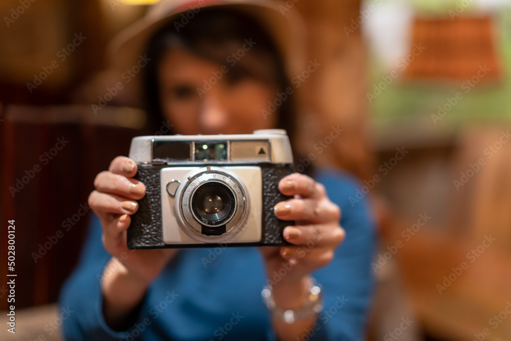A pretty tourist with a hat and a photo camera drinking tea in a cafe, taking some photos with the vintage camera looking at the camera A pretty tourist with a hat and a photo camera drinking tea in a cafe, taking some photos with the vintage camera looking at the camera