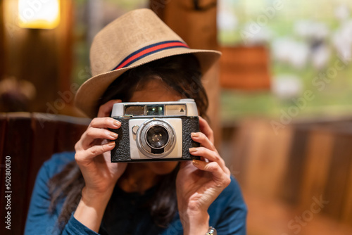 A pretty tourist with a hat and a photo camera drinking tea in a cafe, taking some photos with the vintage camera looking at the camera © unai