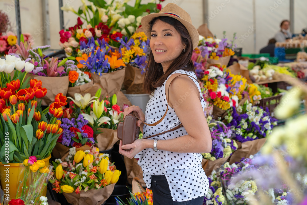 A pretty tourist in a hat visiting a flower market, enjoying spring or summer vacation