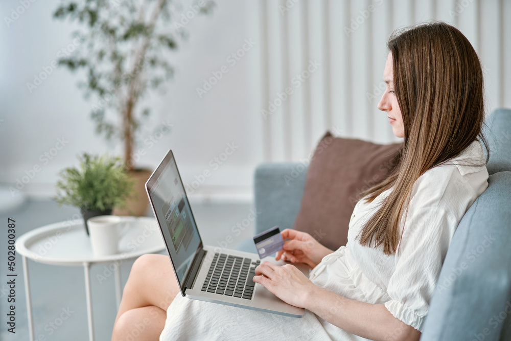 Fototapeta premium smiling woman with a credit card making online purchases while sitting on the couch.