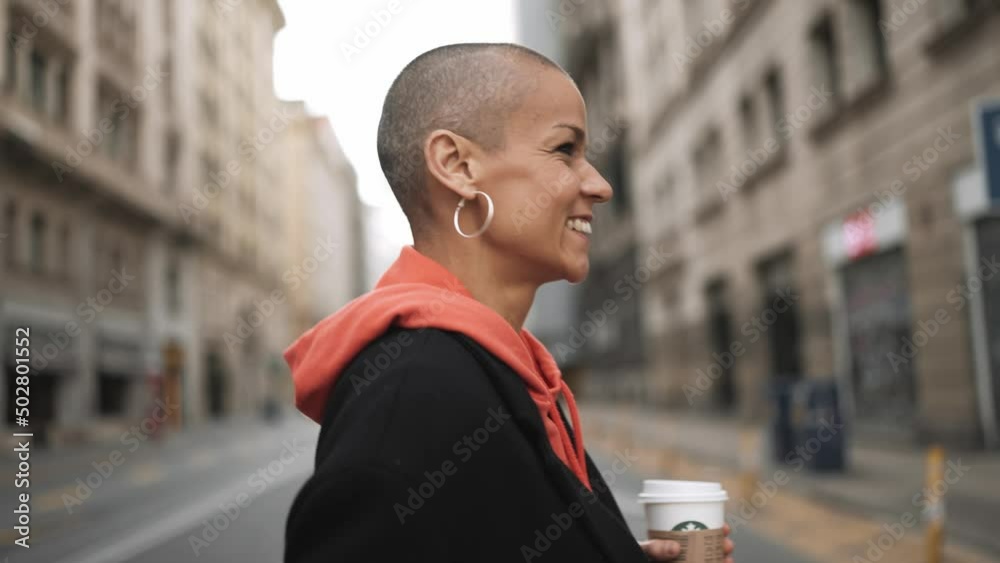 Smiling bald woman walking with cup of coffee on the street Smiling bald woman walking with cup of coffee on the street