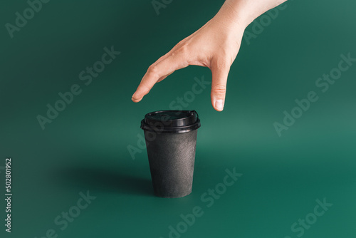 Hand reaching for dark cup on green background.