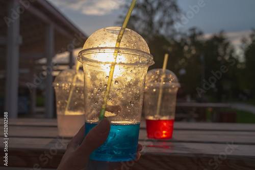 Carbonated water in plastic cups with cocktail tubes in the evening on a summer day in a street cafe © Olga