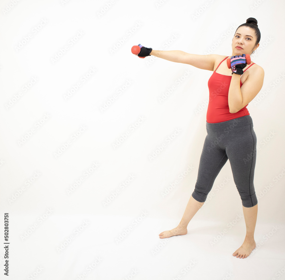 cute athletic woman wearing gray sportswear, red top, practicing boxing, dumbbells, throwing punches forward with right arm, on white background cute athletic woman wearing gray sportswear, red top, practicing boxing, dumbbells, throwing punches forward with right arm, on white background