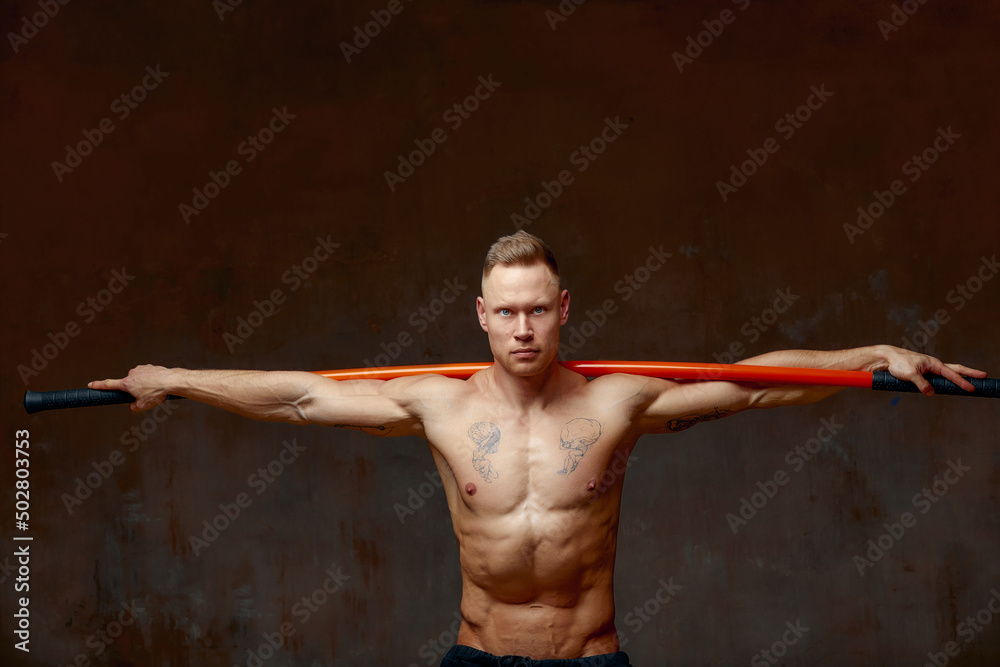 A fighter or karate man, stands in a fighting artificially pose and holds a bamboo stick on gray wall studio background.