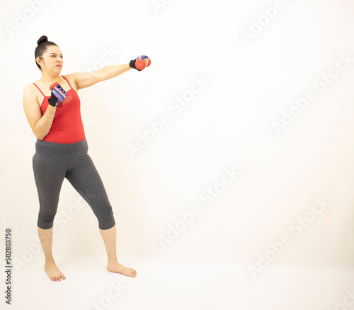 cute athletic woman wearing gray sportswear, red top, practicing dumbbell boxing, angry furious throwing punches to front, on white background