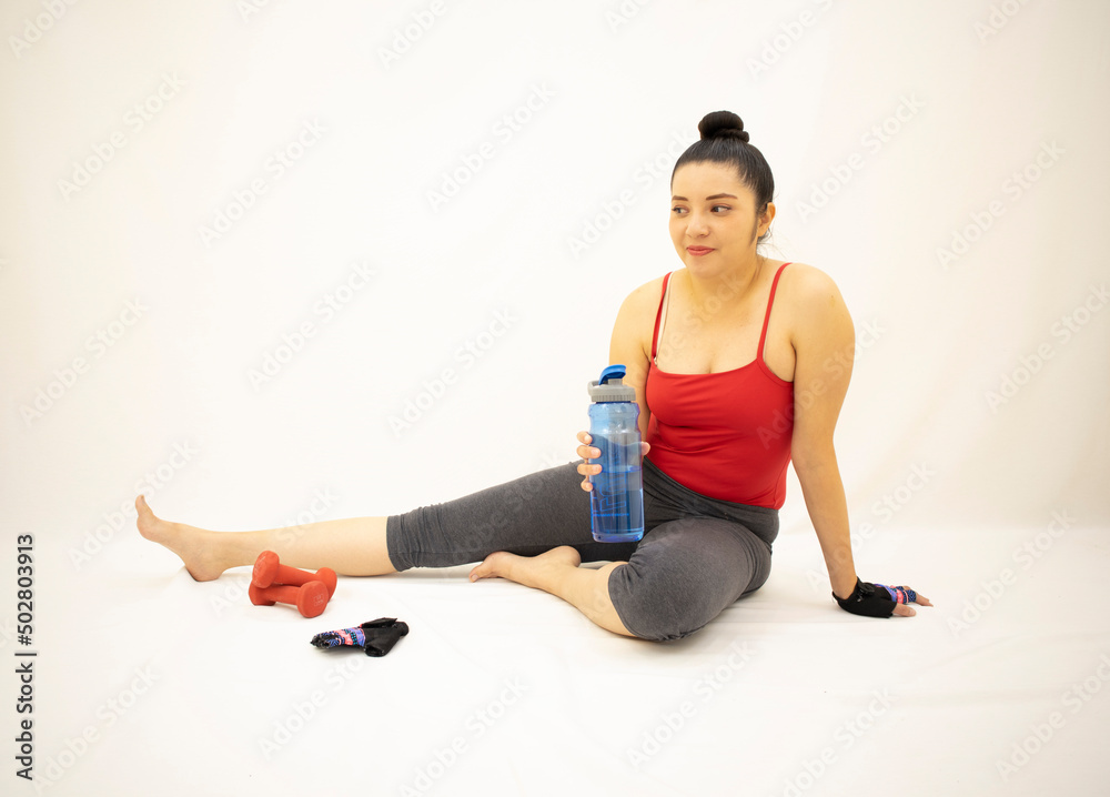 beautiful woman in gray sportswear, red blouse, resting and smiling after exercising whit dumbbells, with one leg stretched, on white background
