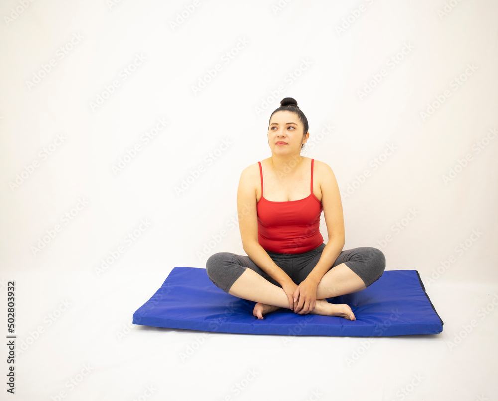 Beautiful white woman in red and gray sportswear, sitting and resting on a blue mat after exercising, on white background. Beautiful white woman in red and gray sportswear, sitting and resting on a blue mat after exercising, on white background.