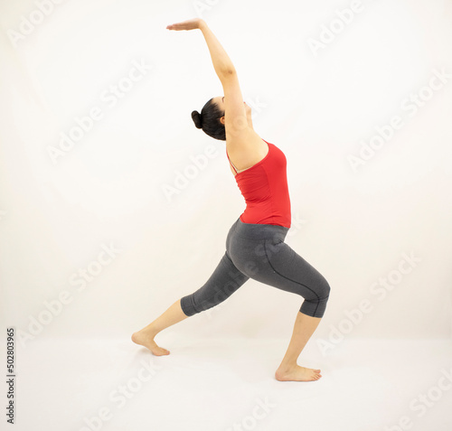 Beautiful white woman in red and gray sportswear, standing barefoot stretching her arms up, on white background.