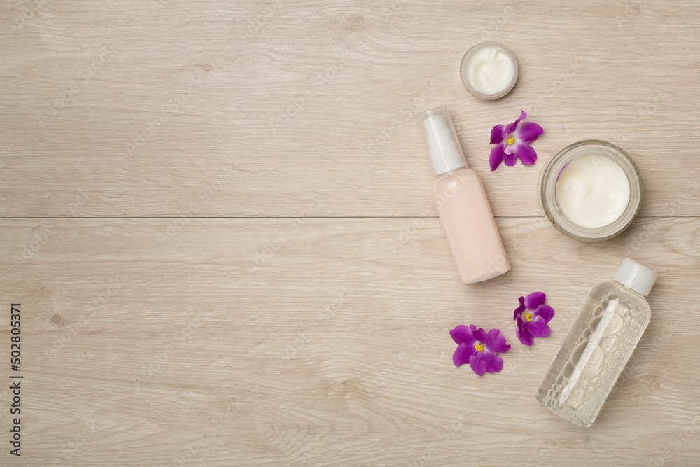 Cosmetic bottles and jars with flowers on wooden background, top view Cosmetic bottles and jars with flowers on wooden background, top view