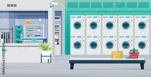 The washing machine is working and the clothes are in the laundry basket in the laundromat.
