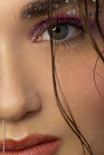 Close-up of the beauty of half a woman's face with creative fashionable make-up of sparkles. Black eyeliner, long eyelashes decorate eyes and lipsand ligth purpure glitter. Well-groomed skin after spa photo