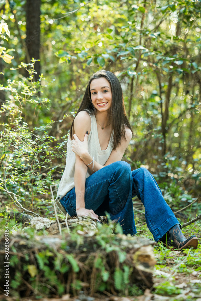 A beautiful happy teenage brunette girl sitting outdoors on a log hapy and smiling with copy space A beautiful happy teenage brunette girl sitting outdoors on a log hapy and smiling with copy space