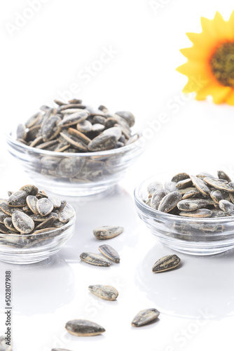 Three bowl of sunflower seeds with sunflower on white background. Vertical format.