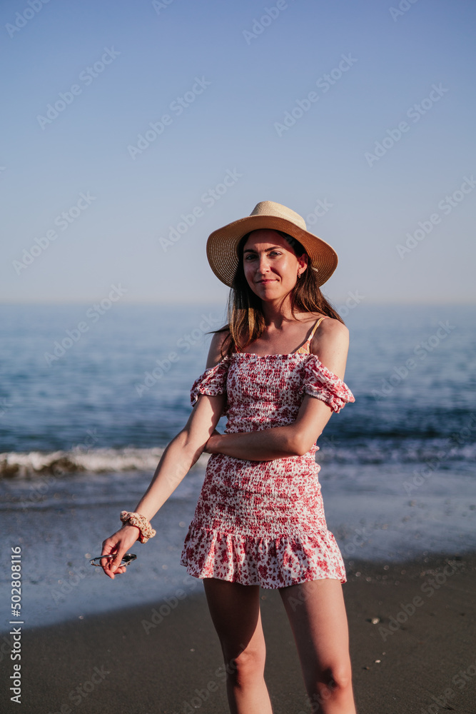 Portrait of beautiful young woman with broad-brimmed hat on the beach at sunset