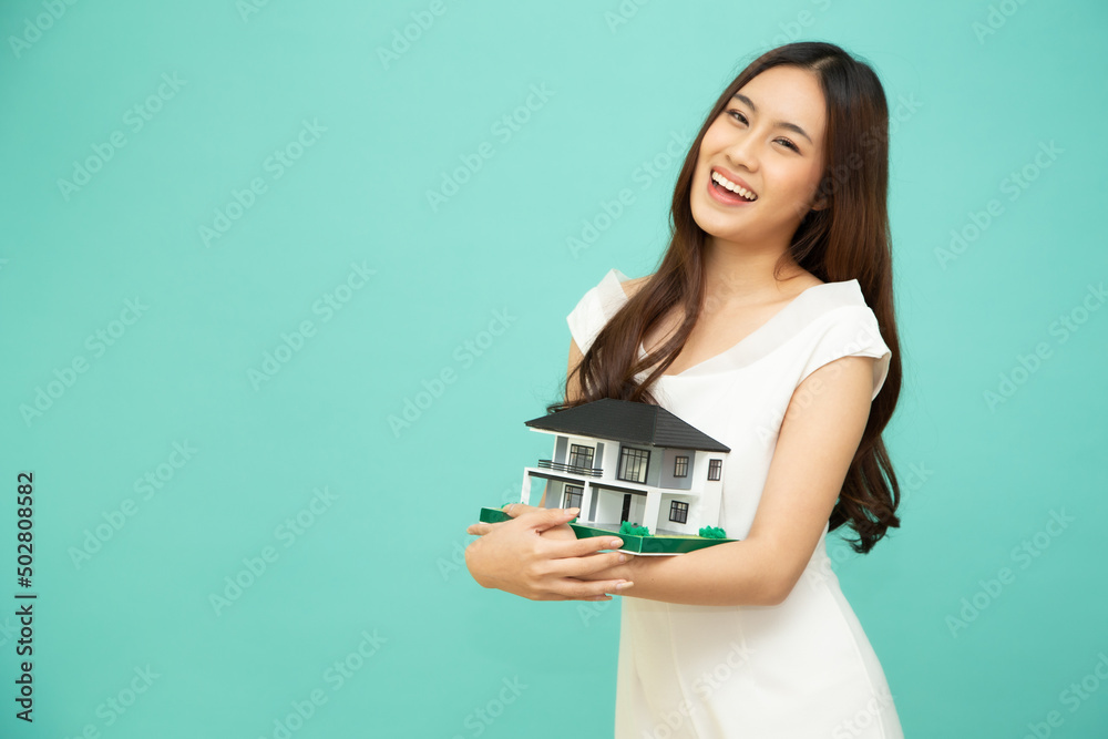 Young Asian woman smiling and holding house sample model isolated over green background, Real estate and home insurance concept Young Asian woman smiling and holding house sample model isolated over green background, Real estate and home insurance concept