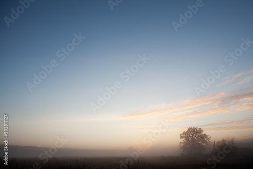 Beautiful foggy sunrise over misty field an early morning. Winter autumn countryside landscape. Fog down in valley, sun and fluffy clouds above horizon