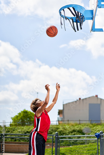 Basketball player performing slam dunk on a street court. Woman in sportswear playing streetball on summer day