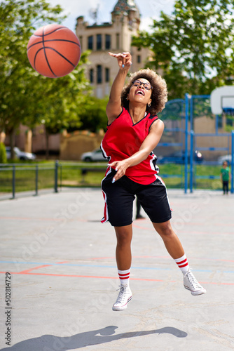 Basketball player performing slam dunk on a street court. Woman in sportswear playing streetball on summer day