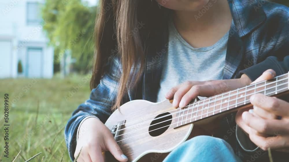 Mujer aprendiendo a tocar ukulele (Guitarra pequeña) en un parque al atardecer.