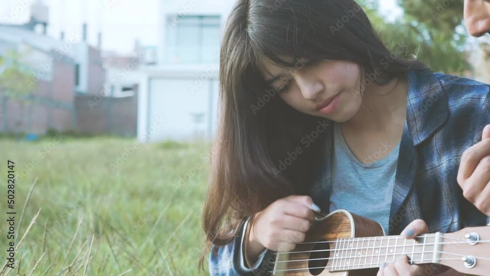 Mujer aprendiendo a tocar ukulele (Guitarra pequeña) en un parque al atardecer.