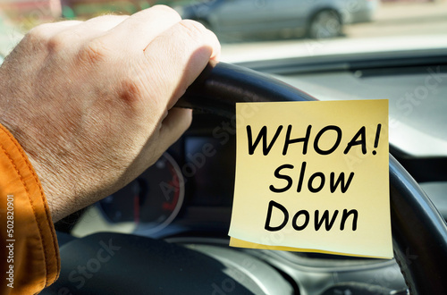 A man holds on to the steering wheel, next to a sticker with the inscription - WHOA Slow Down photo