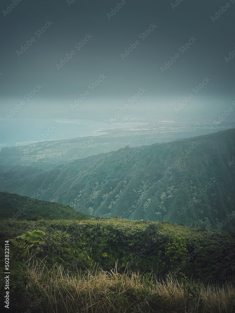 Scenery view from the top of the mountains to the ocean coastline in Hawaii, Oahu island. Moody hiking landscape with foggy, green hills on the horizon and stormy clouds over the bay Scenery view from the top of the mountains to the ocean coastline in Hawaii, Oahu island. Moody hiking landscape with foggy, green hills on the horizon and stormy clouds over the bay