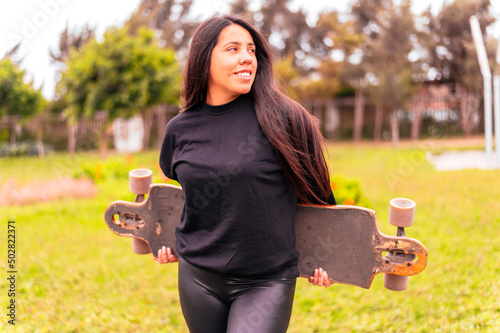 Portrait of smiling young female skateboarder holding her skateboard. Woman with skating boardin the park. photo