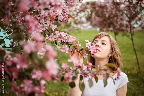 Beautiful young woman smelling blossoming apple branches in spring. © Natalia