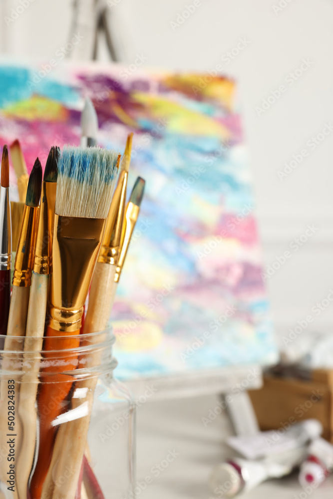 Different paintbrushes in glass on blurred background, closeup. Space for text Different paintbrushes in glass on blurred background, closeup. Space for text