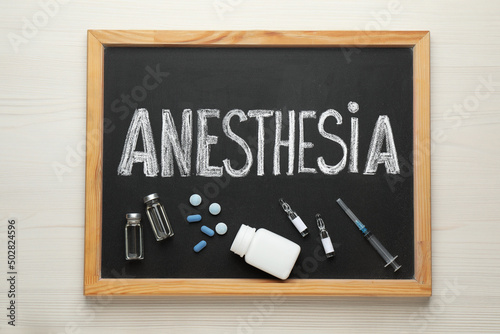 Blackboard with word Anesthesia, syringe and drugs on white wooden table, top view photo