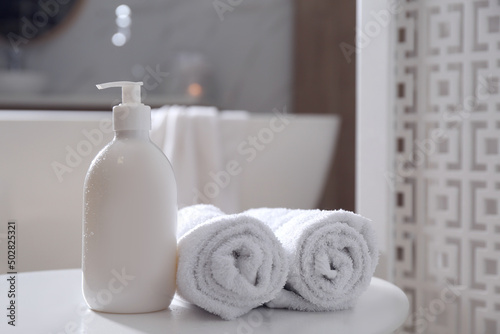 Bottle of shower gel and fresh towels on white table in bathroom. Space for text
