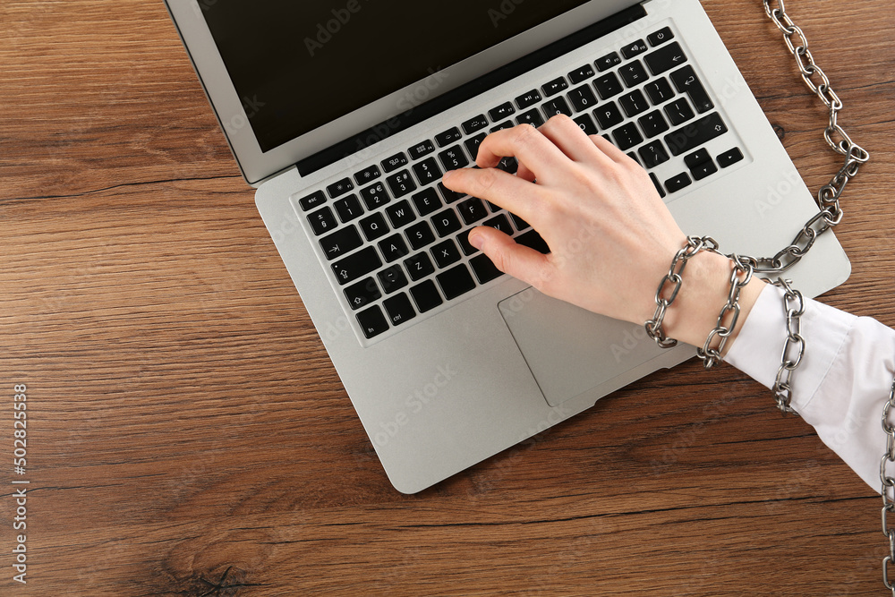 Woman with chained hand typing on laptop at wooden table, top view. Internet addiction Woman with chained hand typing on laptop at wooden table, top view. Internet addiction