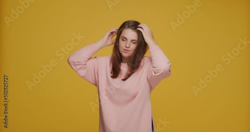 Young girl fix hairs, freshen her makeup, primping, preening up, preparing for dating on yellow studio background