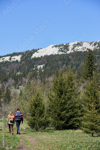 Young couple holding hands and walking along the path towards wild woods and white rocks in the distance, rear view