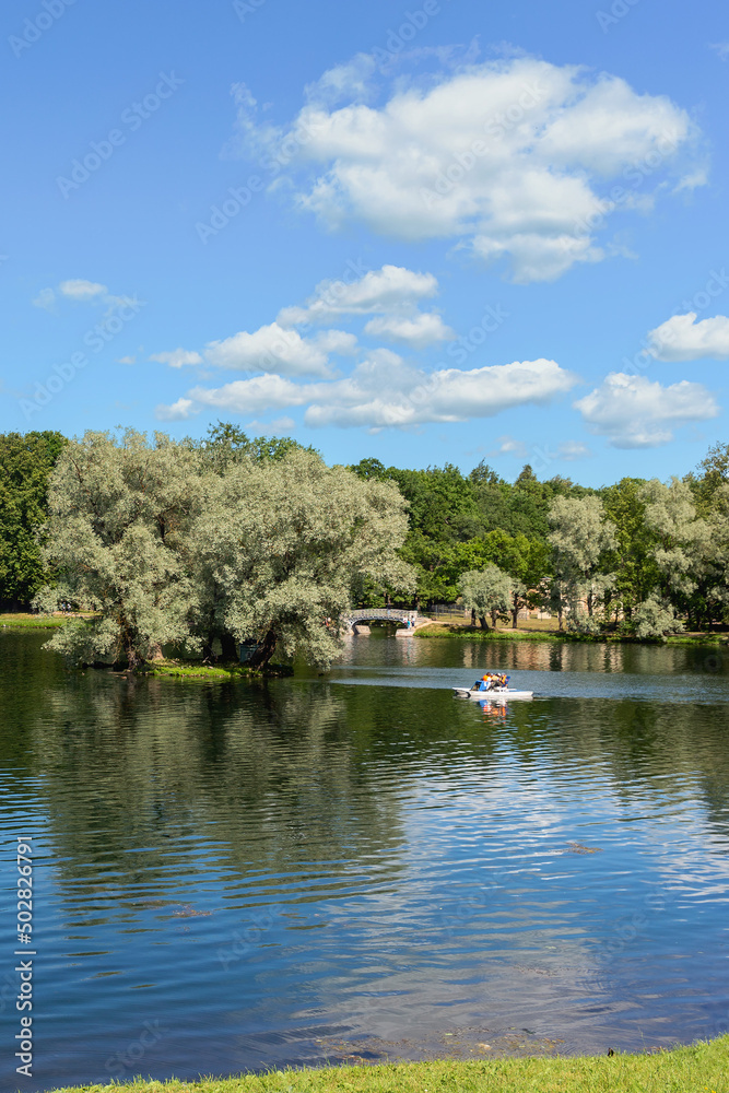 vacationers ride a boat on a forest lake against the backdrop of a park and blue sky