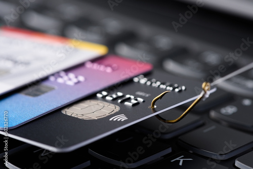 Credit card phishing scam concept. Credit card data theft, card hooked on fishing hook pulled from stack of other cards on keyboard.