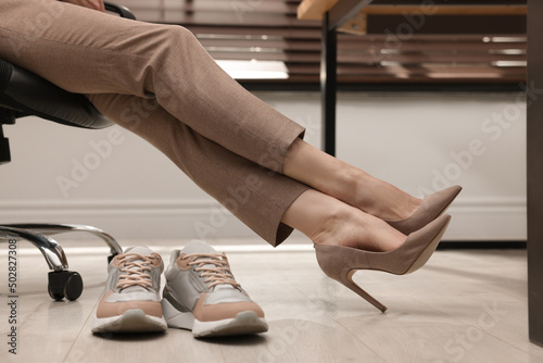 Comfortable sneakers on floor near woman wearing stylish high heeled shoes in office  closeup