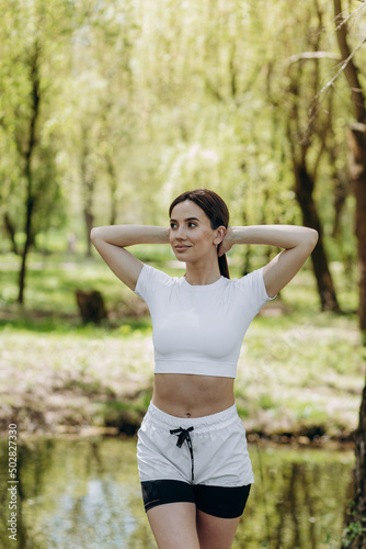 Sporty woman holding in hands shaker, yoga mat and walking to training in park. Beautiful sporty fitness model during outdoor workout.