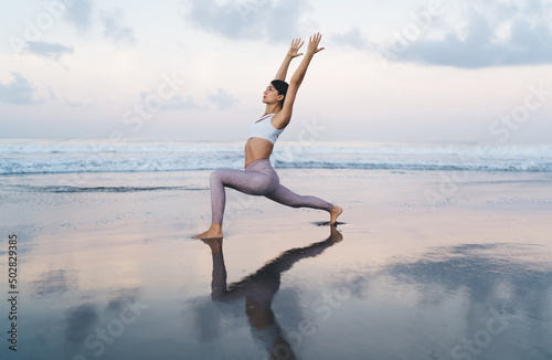 Caucasian woman with perfect body shape strending muscles during warm up concentration at coastline beach  attractive female reaching healthy lifestyle while meditate and breath in asana yoga pose