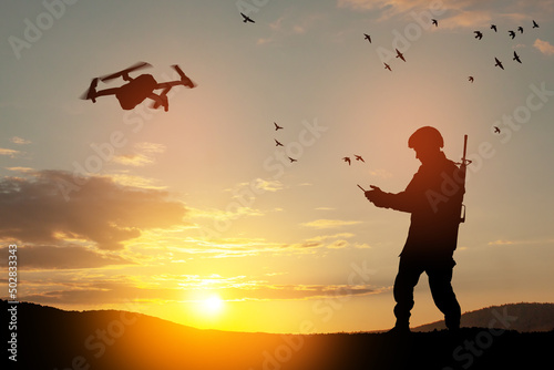 Silhouette of soldier are using drone and laptop computer for scouting during military operation against the backdrop of a sunset. Greeting card for Veterans Day, Memorial Day, Independence Day.