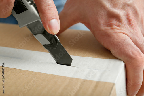 Man using utility knife to open parcel, closeup