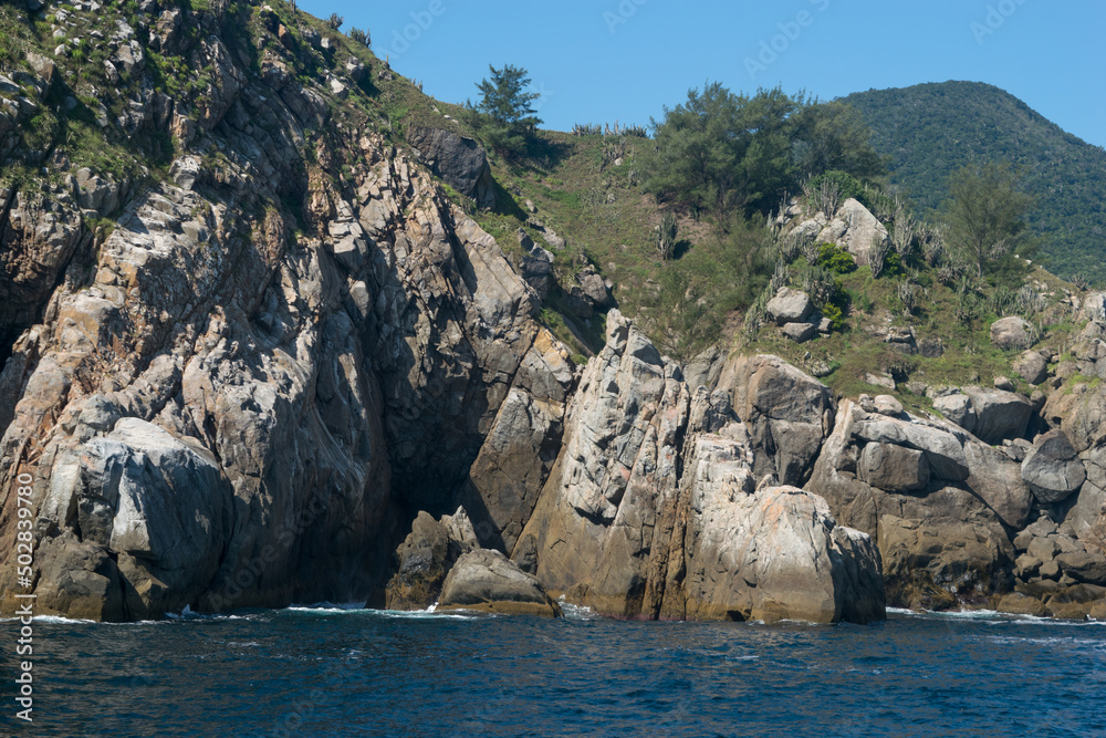 Montanha rochosa a beira do mar e com pequena caverna no meio, localizada na região de Cabo Frio, Rio de Janeiro, Brasil.