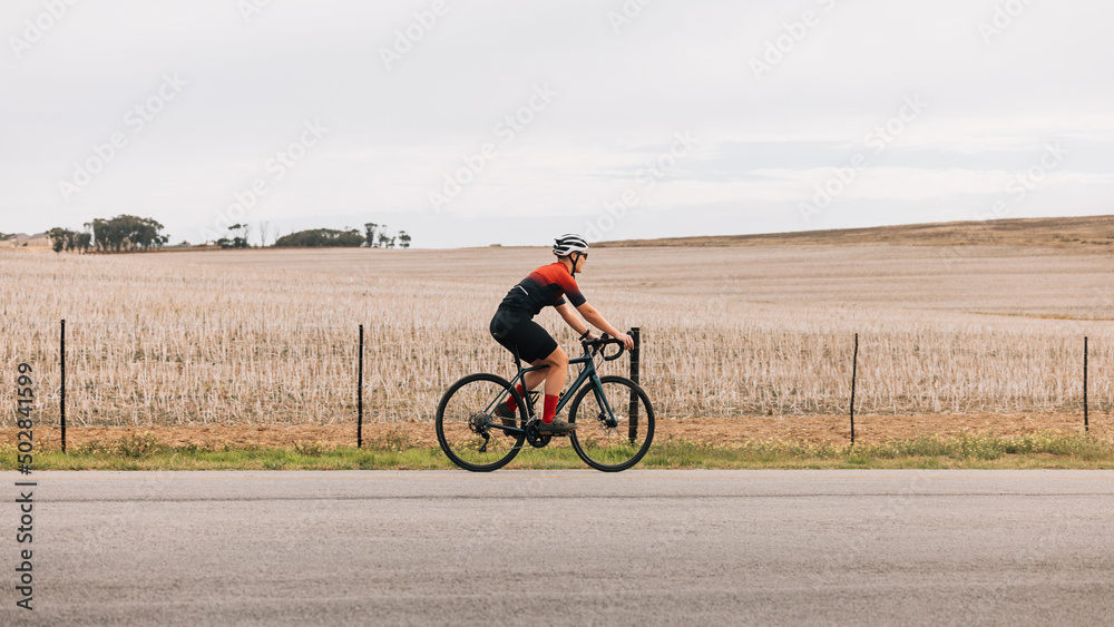 Woman cyclist exercising outdoors on road bike against agriculture field