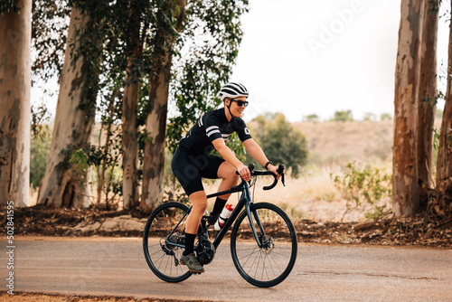 Professional female cyclist in sunglasses and helmet riding bike outdoors