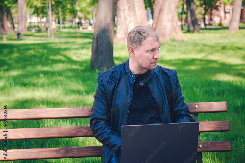 Fototapeta premium Technology, communication, education, copy space. Remote work concept, Man connected on internet outside the house. Concentrated man working on laptop in pleasant atmosphere in park