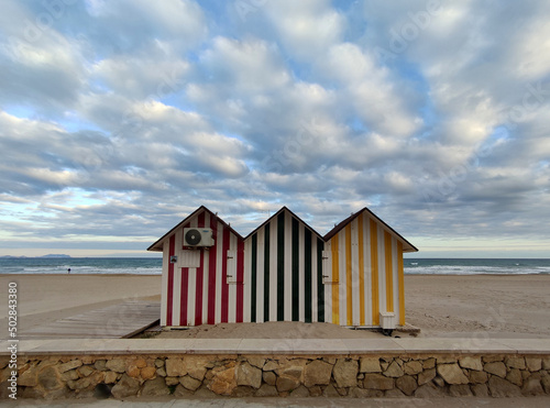 3 casetas de playa a rayas de colores con la playa de fondo y cielo con nubes photo