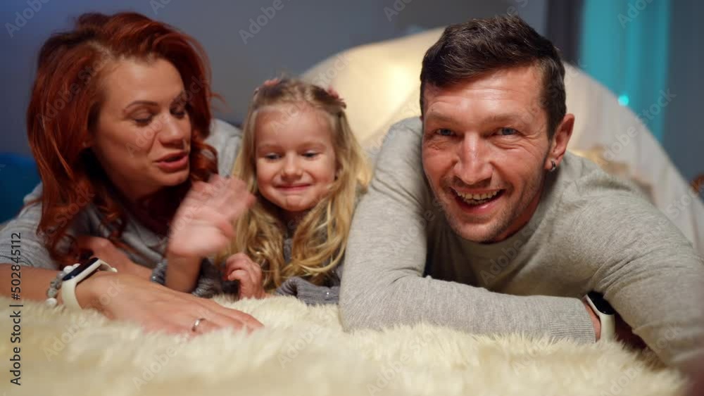 Selfie POV of happy man posing with family waving lying at tent in living room. Positive Caucasian husband wife and daughter smiling talking blogging online. Modern technologies and togetherness Selfie POV of happy man posing with family waving lying at tent in living room. Positive Caucasian husband wife and daughter smiling talking blogging online. Modern technologies and togetherness