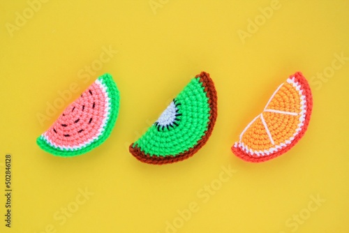 Colourful crochet handmade slices of watermelon, kiwi and orange on yellow background. Summer vacation creative tropical bright minimalistic food concept. Flatlay, top view holiday composition.