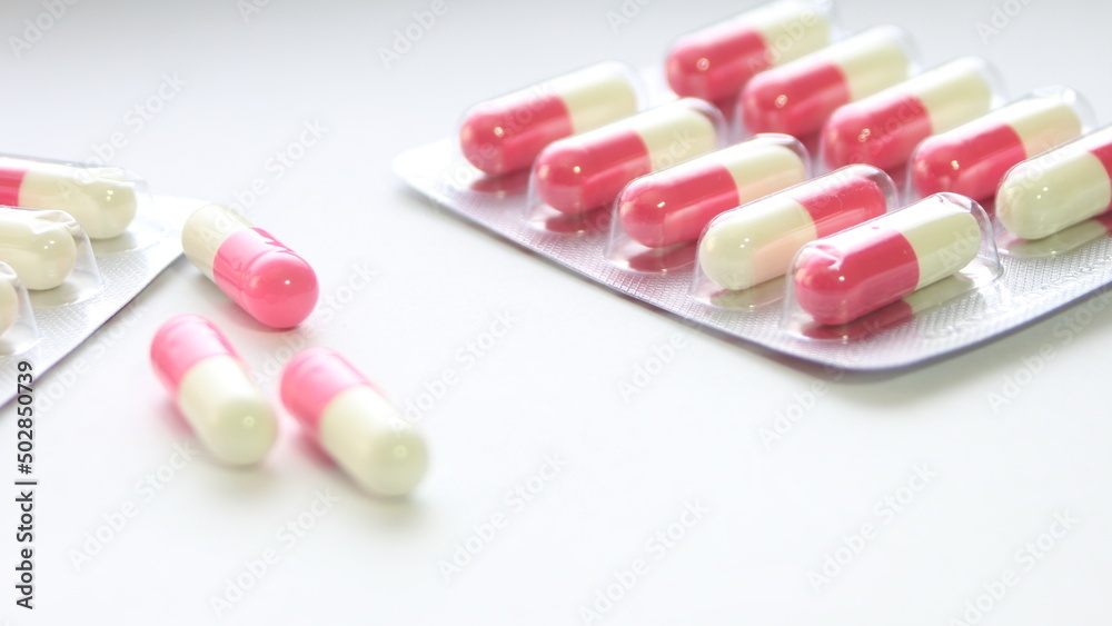 Pink-green pill capsules were placed on a white table. Pink-green pill capsules were placed on a white table.